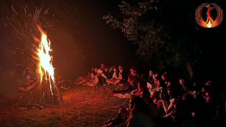 Foc de tabără arzând noaptea, cu participanți în jur